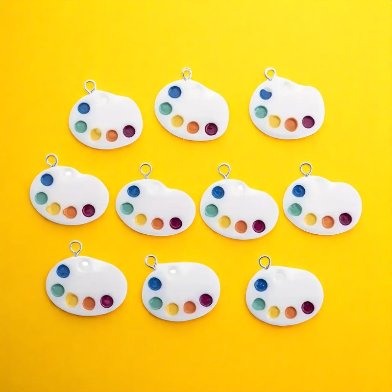 A collection of white paint palette-shaped shoelace charms with multicolored sections and rings attached for accessory purposes, displayed on a yellow background.