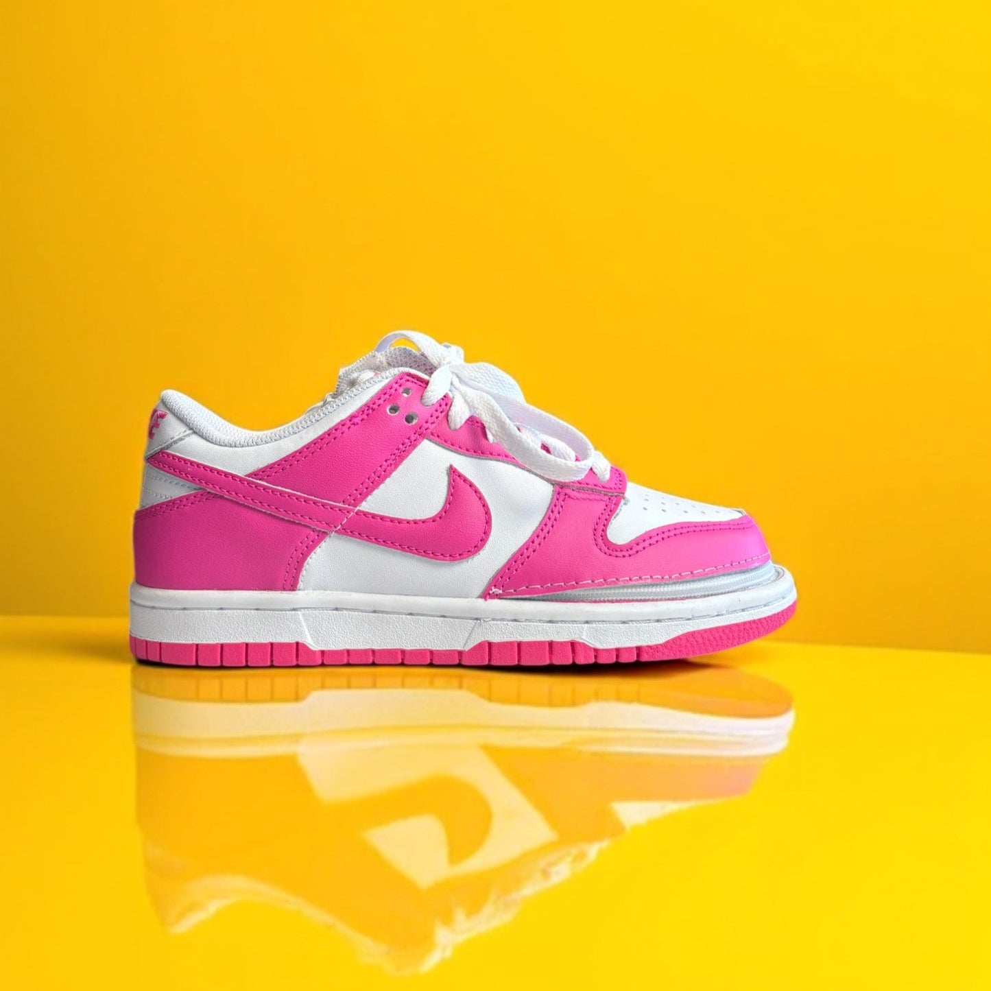 A customized Big Kids' Nike Dunk Low with a zipper, primarily in pink and white colors on a yellow background.