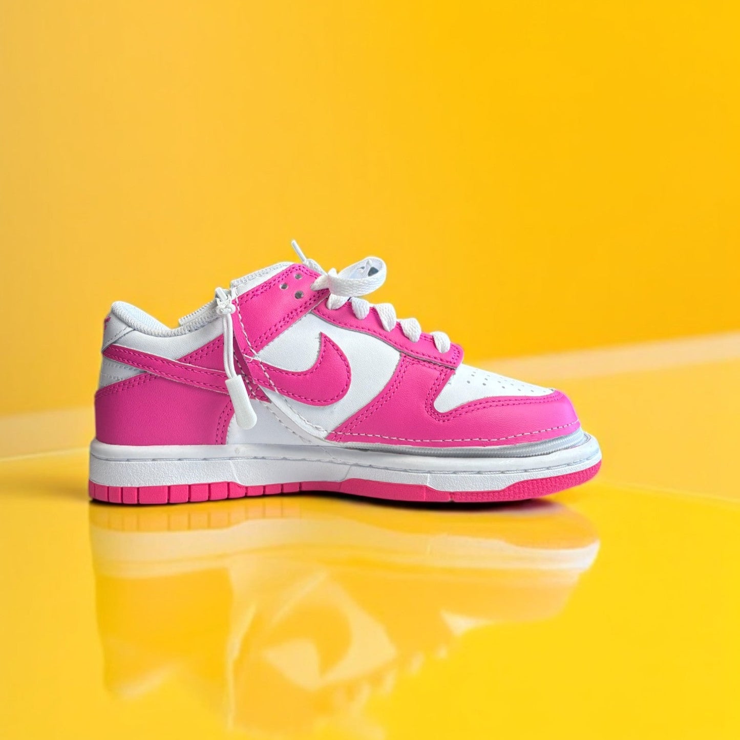 A customized Big Kids' Nike Dunk Low with a zipper, primarily in pink and white colors on a yellow background.