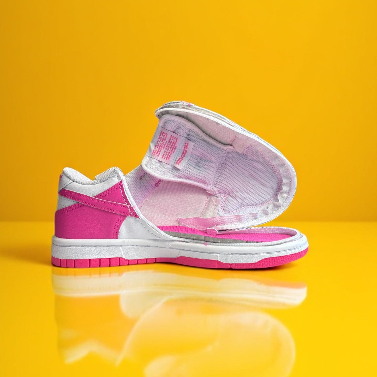 A customized Big Kids' Nike Dunk Low with a zipper, primarily in pink and white colors on a yellow background.