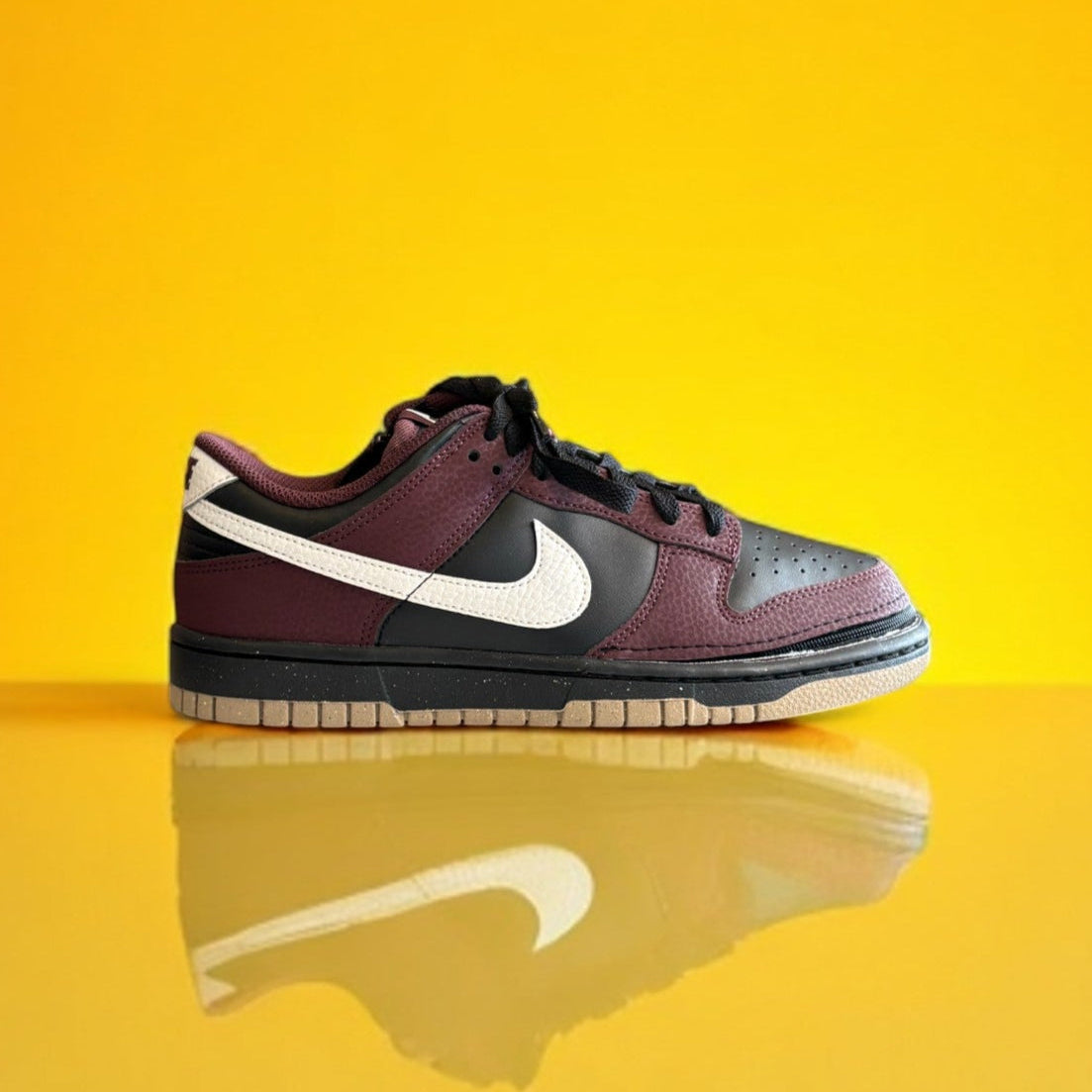 Maroon and black Nike dunk next nature with a zipper on yellow background