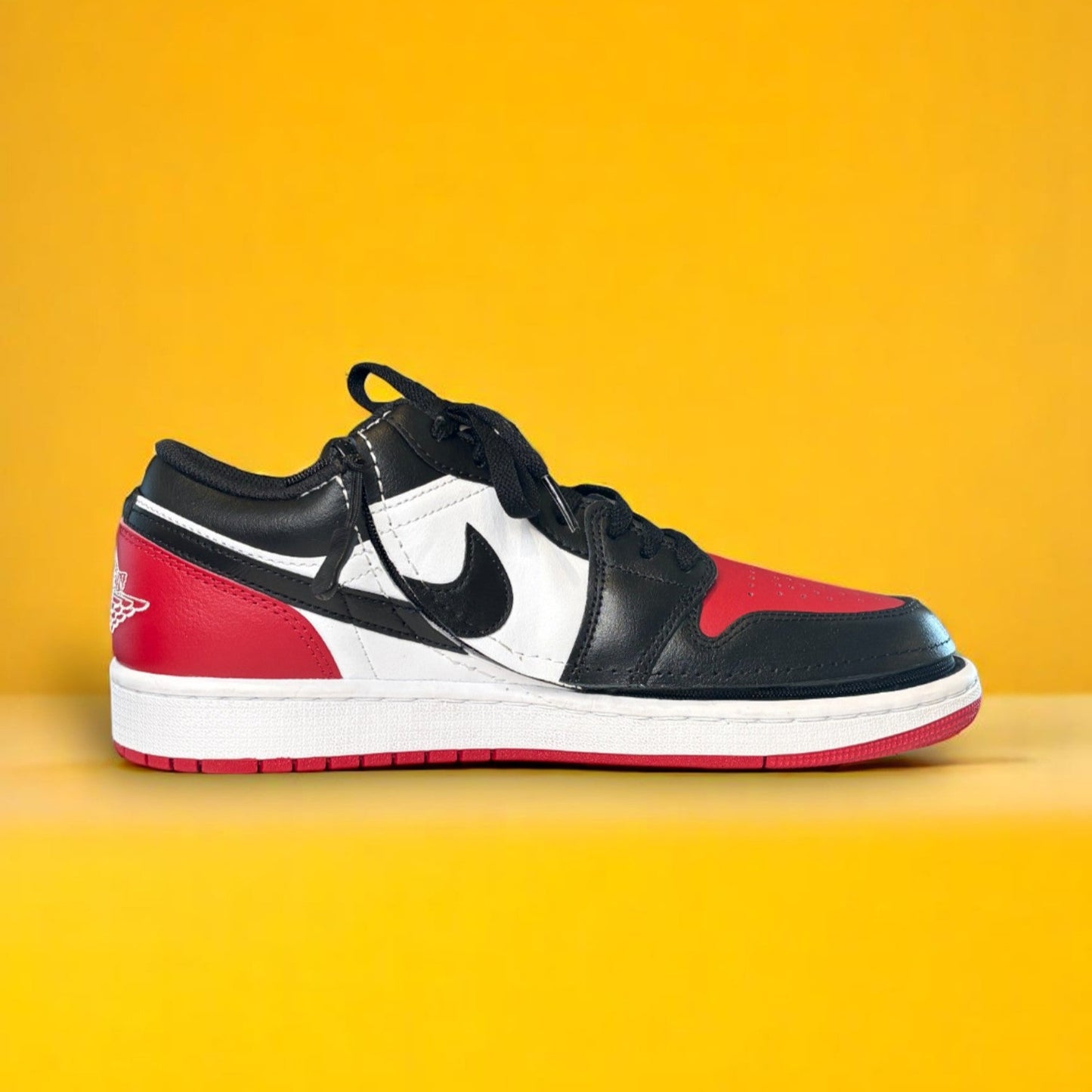Black, white, and red sneaker on a yellow background The shoe has a zipper. The zipper wraps around the shoe allowing it to open fully. The shoe is an Air Jordan 1 Low Top.